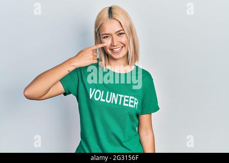 Belle femme blonde portant le t-shirt volontaire pointant du doigt de la main au visage et au nez, souriant gai. Concept de beauté Banque D'Images