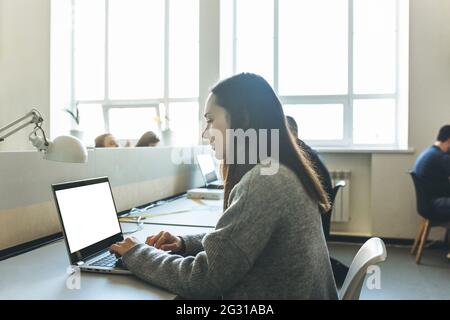 Une fille adulte utilise un ordinateur portable avec un écran blanc vierge pour la maquette Banque D'Images