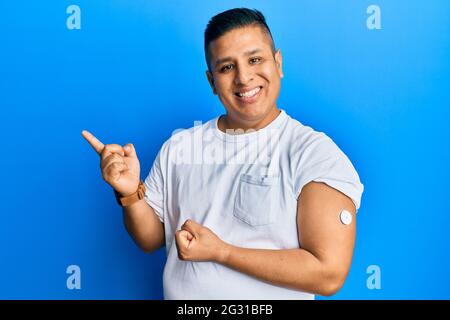 Jeune homme latin utilisant le bouton du glucomètre sourire heureux pointant avec la main et le doigt sur le côté Banque D'Images
