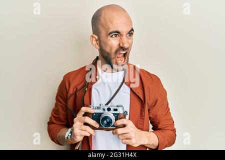 Jeune hispanique tenant une caméra d'époque en colère et folle hurlant frustré et furieux, criant avec colère. Rage et agressif concept. Banque D'Images