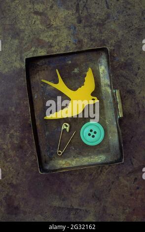Ancienne boîte en laiton contenant une broche jaune d'hirondelle, un bouton vert et une broche de sécurité Banque D'Images