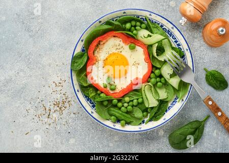 Poivrons rouges farcis avec des œufs, des feuilles d'épinards, des pois verts et des microverts sur une assiette de petit déjeuner sur fond de table gris clair. Vue de dessus. Banque D'Images