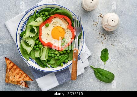 Poivrons rouges farcis avec des œufs, des feuilles d'épinards, des pois verts et des microverts sur une assiette de petit déjeuner sur fond de table gris clair. Vue de dessus. Banque D'Images