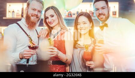 Jeune couple tendance posant avec des verres à cocktail à la fête Banque D'Images