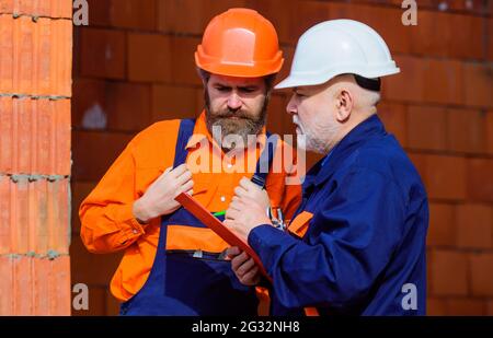 Deux travailleurs avec casques et uniforme de constructeur dans le chantier de construction. Des constructeurs professionnels sur le lieu de travail Banque D'Images