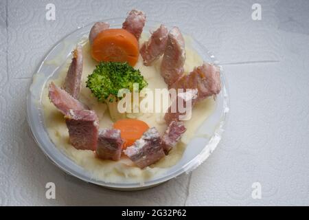 Cuisine britannique artistique, sur fond de papier de cuisine blanc Uni. Présenté dans un bac rond en plastique avec des légumes colorés et un anneau de tranches de gammon Banque D'Images