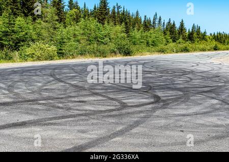 Nombreuses marques de dérapage sur une route de campagne. Ils couvrent complètement cette partie de la route, et semblent de nature aléatoire et circulaire. Arbres et ciel bleu visibles. Banque D'Images