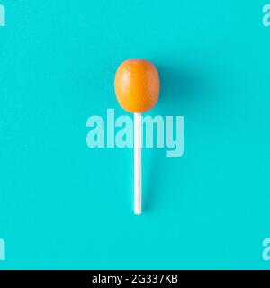 Kumquat fruit petites oranges sur un bâton de Lollipop sur fond bleu turquoise. Concept de nourriture aux agrumes d'été. Style de photographie minimal. Banque D'Images