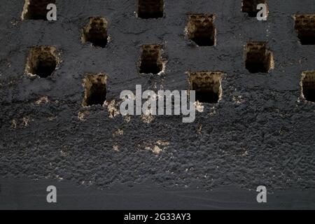Gros plan d'un mur de briques peint en noir qui a des trous dans sa structure qui agissent comme des évents Banque D'Images