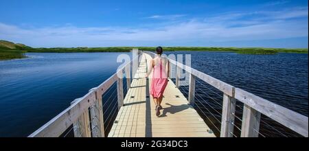 Une femme vêtue d'une robe rose parcourt la promenade flottante au parc national de l'Île-du-Prince-Édouard. Banque D'Images