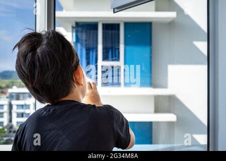 Le concept de nettoyage d'appartement à la maison. Essuyage et mousse sur la fenêtre par le jeune garçon. Vue de derrière. Banque D'Images