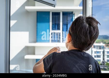 Le concept de nettoyage d'appartement à la maison. Un garçon sur la fenêtre et essuyent avec un chiffon. Vue de l'arrière. Banque D'Images