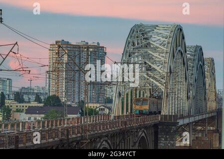 Le train se déplace à l'horaire après le coucher du soleil sur l'ancien pont ferroviaire, Kiev, Ukraine Banque D'Images