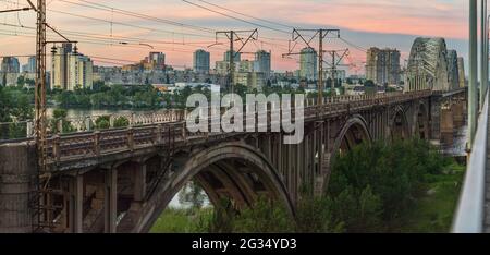 Le train se déplace à l'horaire après le coucher du soleil sur l'ancien pont ferroviaire, Kiev, Ukraine Banque D'Images