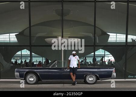 Le gardien de parking Lonrenzo Franklyn se penche contre un Lincoln Continental 1964 décapotable alors qu'il attend que les clients arrivent à l'hôtel TWA de l'aéroport international JFK, dans le quartier Queens de New York City, NY, le 13 juin 2021. Situé dans l'ancien centre de vol TWA conçu par l'architecte Eero Saarinen et ouvert en 2019, l'hôtel évoque un style architectural des années 1960, l'hôtel accueille les visiteurs d'une journée et les passagers de passage à New York, où les gens peuvent se détendre et prendre une heure plus de se baigner dans une piscine chauffée à débordement, les réservations sont nécessaires pour prendre des distances sociales. (Photo d'Antho Banque D'Images