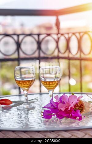 Gros plan de la glass de vin avec des fleurs roses de bougainvilliers sur une table en verre. Concept de rafraîchissement. Fleurs surréalistes d'été. Arrière-plan ensoleillé en été. Photo de haute qualité Banque D'Images