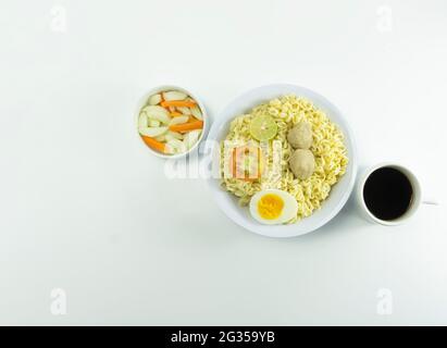 Nouilles chaudes servies avec tomates fraîches et boulettes de viande sur un bol rond blanc et cornichons sur un bol blanc sur fond blanc Banque D'Images