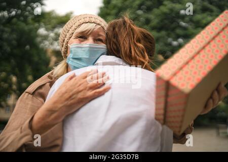 Jeune femme donnant la grand-mère présente et embrassant à l'extérieur dans la ville, la vie après la vaccination Covid-19. Banque D'Images