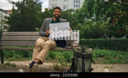 Portrait d'un jeune homme joyeux tenant une bannière à l'extérieur de la ville, campagne de vaccination Covid-19. Banque D'Images