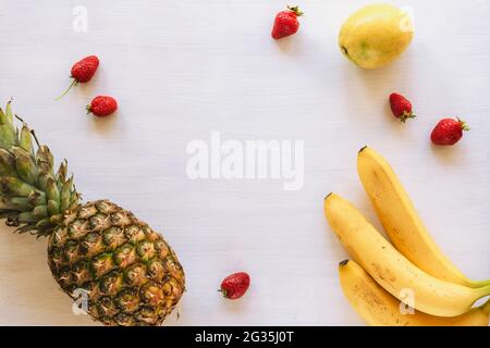 Ananas, bananes, citron et fraises sur une table en bois blanc avec espace pour les copies, vue du dessus. Banque D'Images