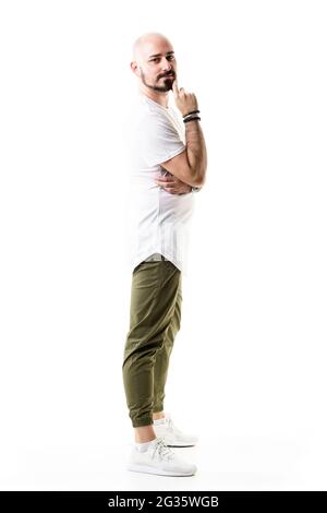 Joyeux jeune homme dans un pantalon vert olive et un t-shirt blanc posant avec la main sur le menton. Longueur totale du corps isolée sur fond blanc Banque D'Images