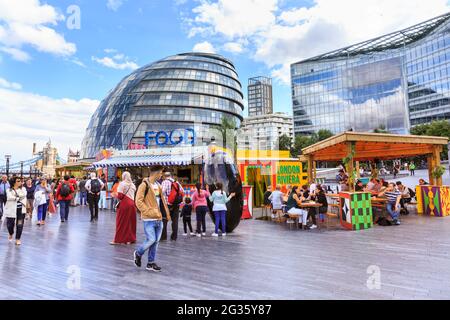 Les gens apprécient la nourriture d'un stand de pop up extérieur à More London, au soleil d'été avec Tower Bridge et City Hall en arrière-plan, Londres, Angleterre Banque D'Images