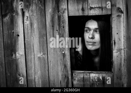 Une jeune femme dans un bâtiment en bois ща fenêtre. Photo en noir et blanc. Banque D'Images