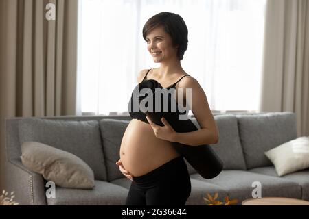 Femme enceinte souriante dans des vêtements de sport noirs tenant un tapis de yoga Banque D'Images