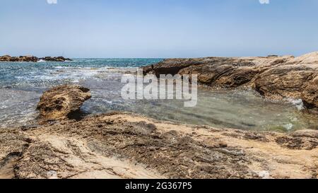 L'eau de la mer Méditerranée entre entre les rochers d'une crique à Alicante. Il y a des vagues et de la mousse. En arrière-plan, vous pouvez voir un pêcheur Banque D'Images