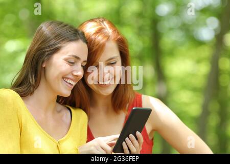 Deux femmes heureuses qui s'occupent d'un smartphone dans une forêt verte ou dans un parc Banque D'Images