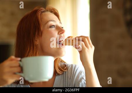 Bonne femme mangeant et buvant pour le petit déjeuner dans le salon à la maison Banque D'Images