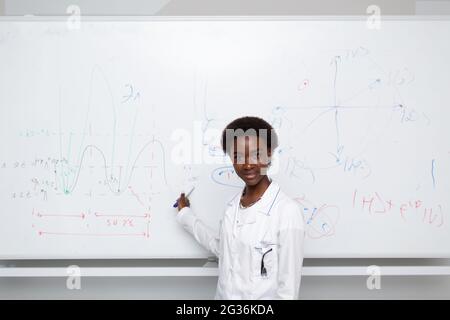 Femme afro-américaine enseignante de mathématiques écrivant sur le tableau noir avec marqueur. Banque D'Images