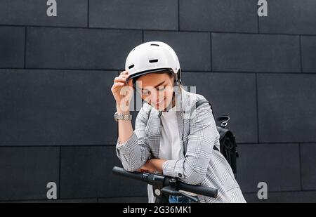 Bonne femme d'affaires dans le casque de vélo penchée sur le guidon du pouleur électrique regardant vers le bas Banque D'Images