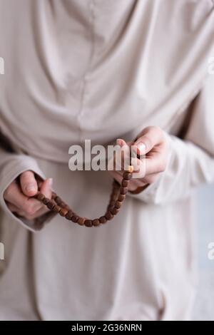 foyer sélectif de rosaire dans les mains d'une femme musulmane floue priant à la maison, vue rognée Banque D'Images