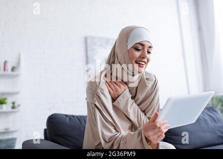 femme arabe joyeuse dans le hijab utilisant la tablette numérique à la maison Banque D'Images