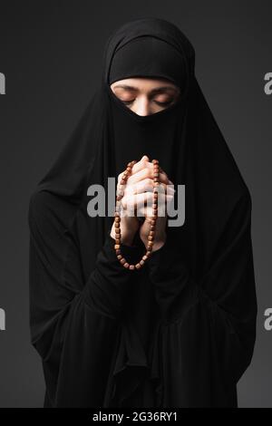 jeune femme musulmane aux yeux fermés tenant le rosaire tout en priant isolée sur le noir Banque D'Images