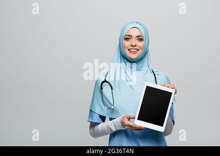 médecin musulman souriant tenant une tablette numérique avec écran vierge isolé sur gris Banque D'Images