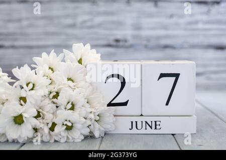 Blocs de calendrier en bois blanc avec la date du 27 juin et des pâquerettes blanches. Mise au point sélective avec arrière-plan flou. Banque D'Images