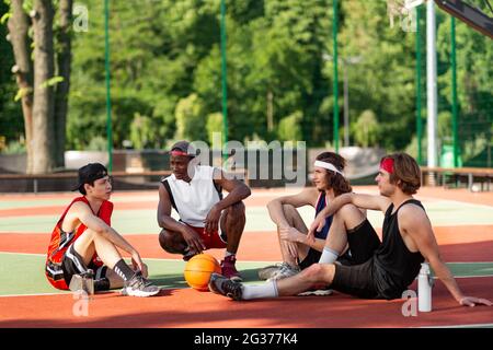 Les sportifs multiraciaux du millénaire communiquent pendant leur repos sur le terrain de basket-ball à l'extérieur, dans un espace vide Banque D'Images