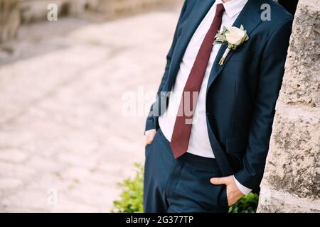 Le marié dans le costume avec une cravate rouge et une boutonnière avec rose blanche sur la rue de la vieille ville, en gros plan Banque D'Images