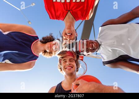 Groupe de joueurs de basket-ball heureux de mettre leur tête ensemble dans l'unité à l'extérieur, vue de dessous Banque D'Images