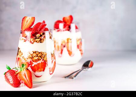 Petit déjeuner sain composé de parfaits aux fraises, de yaourts et de muesli frais en verres. Banque D'Images