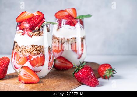 Petit déjeuner sain composé de parfaits aux fraises, de yaourts et de muesli frais en verres. Banque D'Images