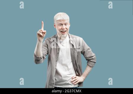 Ouah, eureka. Jeune drôle albino gars pointant le doigt vers le haut, a trouvé la solution à son problème, debout sur fond bleu Banque D'Images