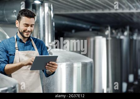 Un jeune homme travaille à l'usine de bière. Brasseur, équipement industriel et dispositif numérique intelligent moderne à la brasserie Banque D'Images