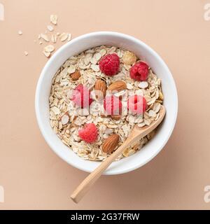 Sécher le muesli d'avoine avec les amandes et les framboises fraîches dans un bol sur fond beige, vue du dessus. Concept de perte de poids, forme physique style de vie, manger propre Banque D'Images