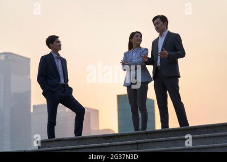 une équipe de cadres d'entreprise asiatiques se tenant sur une plate-forme discutant au crépuscule avec un arrière-plan de la ville Banque D'Images