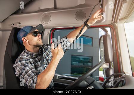 Semi-conducteur de camion caucasien parlant par radio CB à l'intérieur de sa cabine de camion. Thème transport et communication. Banque D'Images