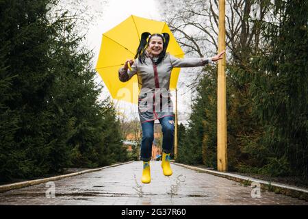 Heureuse senior gaie mature, âgée, femme à la retraite avec parapluie jaune profitant de la vie au jour de pluie dans le parc. Profitez de chaque instant et de la vie Banque D'Images