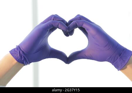 Le médecin en gants bleus dépeint un coeur avec ses mains Banque D'Images